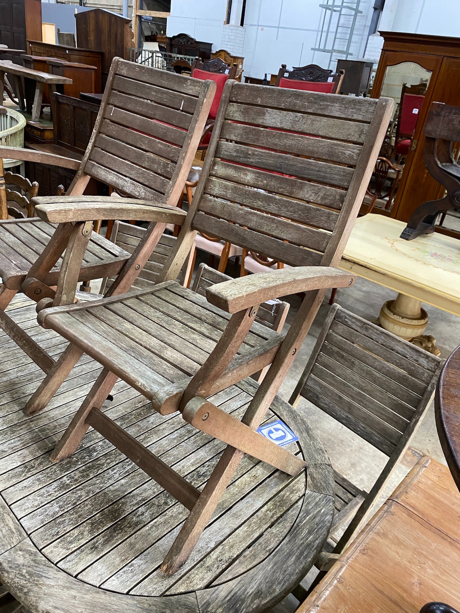 A weathered teak folding oval garden table, length 150cm, depth 91cm, height 74cm together with eight assorted chairs (2 carvers, 6 singles) *Please note the sale commences at 9am.